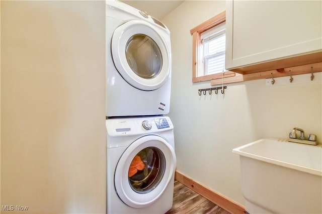 laundry room with laundry area, wood finished floors, a sink, stacked washer and clothes dryer, and baseboards