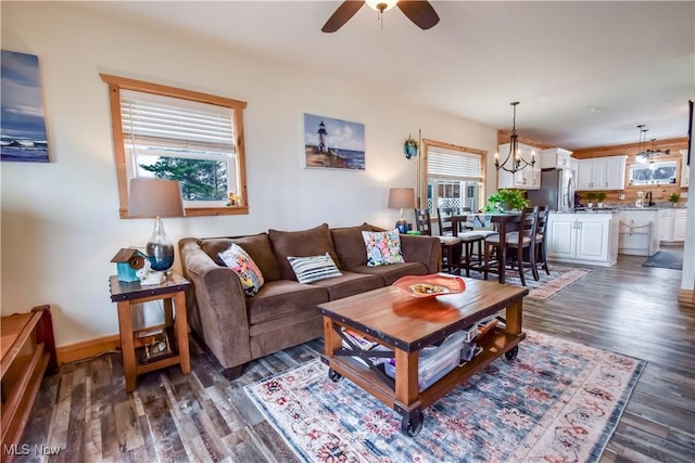living area with ceiling fan with notable chandelier, baseboards, and dark wood-style floors