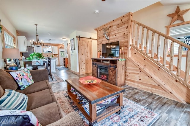 living area with stairs, a barn door, a notable chandelier, and wood finished floors