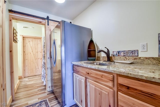 kitchen with light wood-style flooring, freestanding refrigerator, light stone countertops, a barn door, and a sink