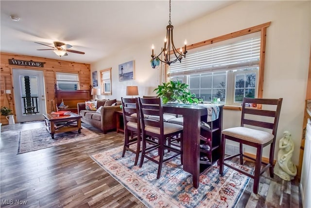 dining room featuring wooden walls, visible vents, wood finished floors, and ceiling fan with notable chandelier