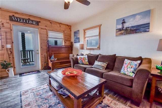 living area featuring wooden walls, a ceiling fan, and wood finished floors