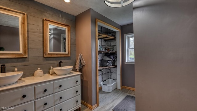 full bathroom featuring a sink, baseboards, double vanity, and wood finished floors