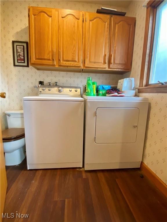 clothes washing area featuring wallpapered walls, dark wood-style flooring, cabinet space, and washer and clothes dryer