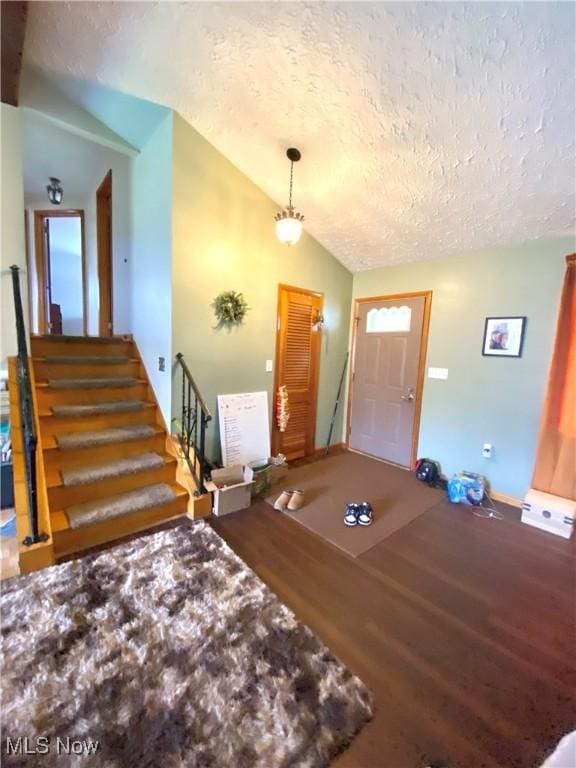 foyer entrance featuring baseboards, a textured ceiling, wood finished floors, stairs, and vaulted ceiling