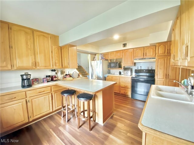 kitchen with a peninsula, under cabinet range hood, light brown cabinets, and stainless steel appliances