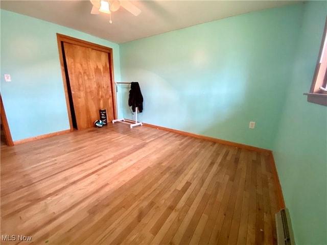 unfurnished bedroom featuring baseboard heating, wood finished floors, baseboards, and a closet