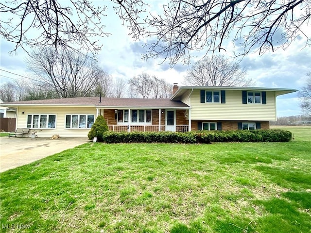 tri-level home with a chimney, covered porch, and a front lawn