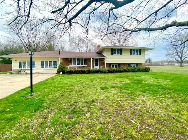tri-level home featuring a front yard, covered porch, driveway, and a chimney