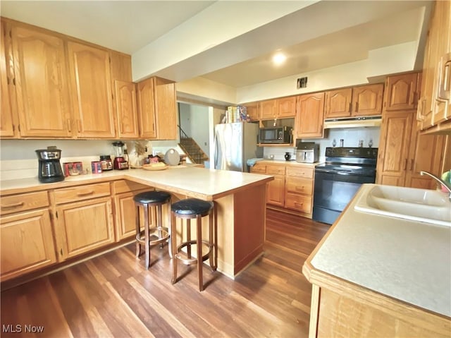 kitchen with a peninsula, freestanding refrigerator, black electric range, under cabinet range hood, and a sink