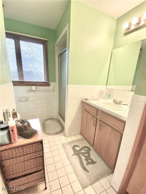 bathroom with vanity, a stall shower, tile patterned flooring, a wainscoted wall, and tile walls