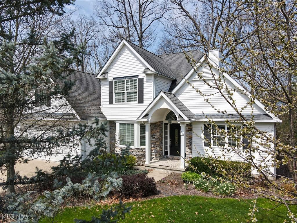 traditional-style home with a chimney, a shingled roof, and stone siding