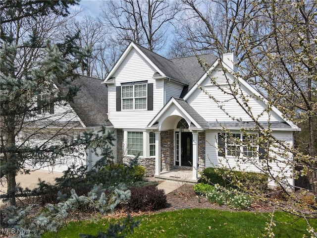 traditional-style home with a chimney, a shingled roof, and stone siding