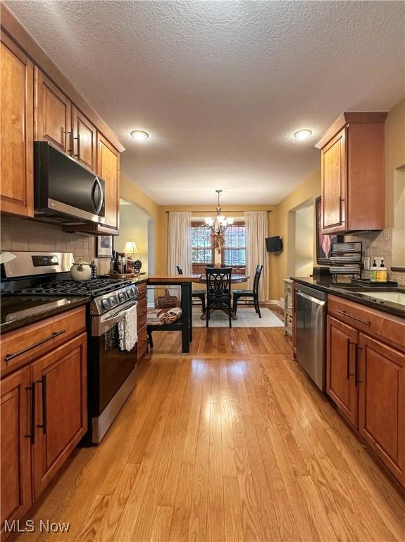 835 John St, Niles, OH 44446 - kitchen featuring tasteful backsplash, light wood-style flooring, dark countertops, brown cabinetry, and stainless steel appliances
