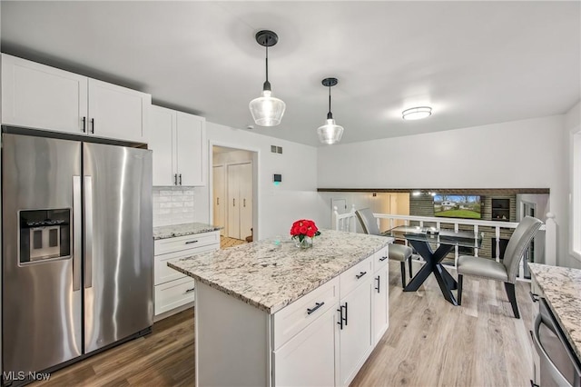 kitchen featuring tasteful backsplash, white cabinets, wood finished floors, light stone countertops, and stainless steel appliances
