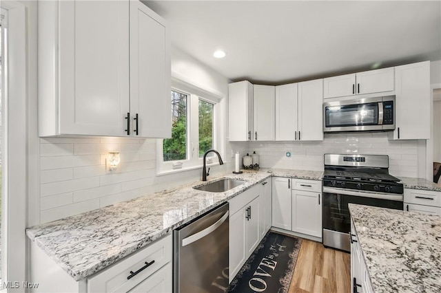 kitchen with a sink, white cabinets, appliances with stainless steel finishes, and wood finished floors