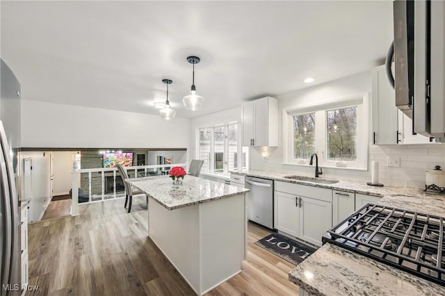 kitchen with light stone counters, a sink, stainless steel dishwasher, a kitchen island, and decorative backsplash