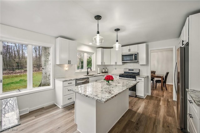 kitchen featuring white cabinetry, backsplash, light stone countertops, appliances with stainless steel finishes, and a sink