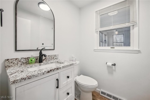 bathroom with vanity, visible vents, toilet, baseboard heating, and wood finished floors
