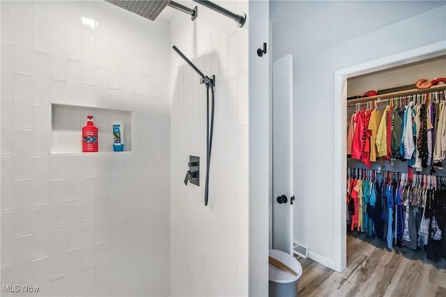 bathroom with tiled shower, wood finished floors, baseboards, and a spacious closet
