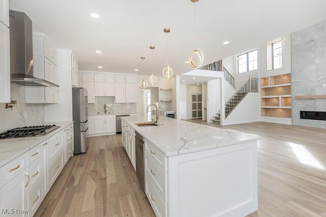 2762 Rocky Ridge Dr, Westlake, OH 44145 - kitchen with wall chimney exhaust hood, a sink, appliances with stainless steel finishes, white cabinetry, and light wood-style flooring