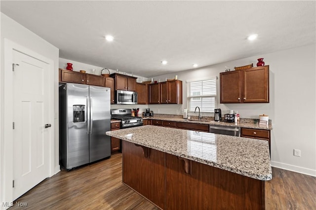 kitchen featuring dark wood finished floors, a kitchen island, light stone counters, a sink, and stainless steel appliances