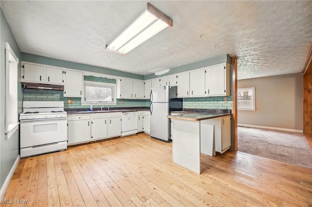 kitchen with white appliances, a peninsula, under cabinet range hood, dark countertops, and decorative backsplash