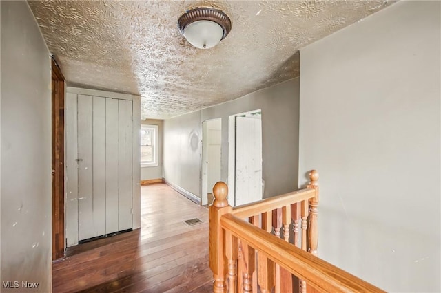 hall featuring visible vents, baseboards, an upstairs landing, hardwood / wood-style flooring, and a textured ceiling