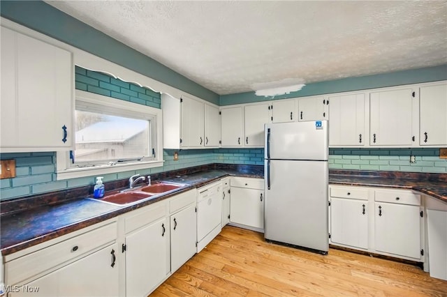 kitchen featuring white appliances, white cabinetry, backsplash, dark countertops, and a sink