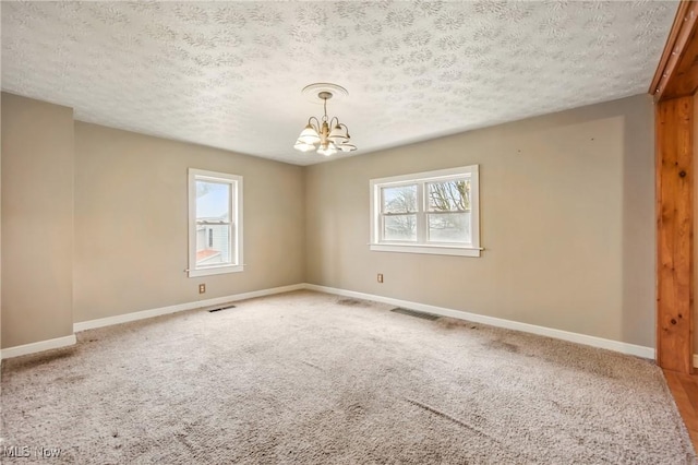 spare room with a chandelier, a healthy amount of sunlight, baseboards, and visible vents
