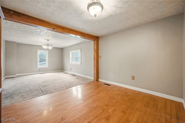 unfurnished room featuring light wood-style flooring, baseboards, an inviting chandelier, and a textured ceiling