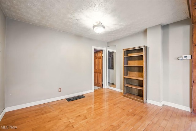 spare room featuring light wood-style floors, baseboards, and a textured ceiling