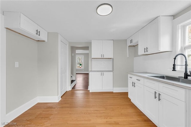 1244 W 69th St, Cleveland, OH 44102 - kitchen featuring baseboards, light wood-style flooring, light countertops, white cabinets, and a sink