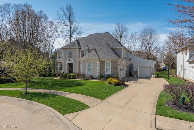 french country inspired facade with a front yard, a shingled roof, stone siding, a garage, and driveway