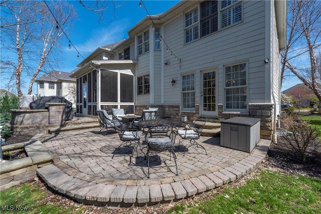 back of property featuring a sunroom, a patio, and stone siding