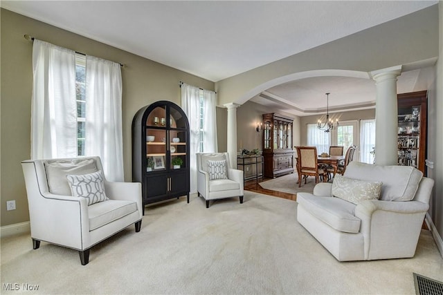living area with a chandelier, arched walkways, ornate columns, and light colored carpet