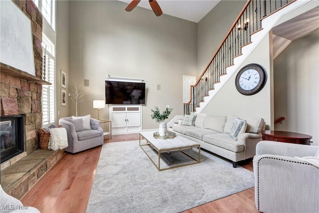 living room with a high ceiling, ceiling fan, a fireplace, wood finished floors, and stairs
