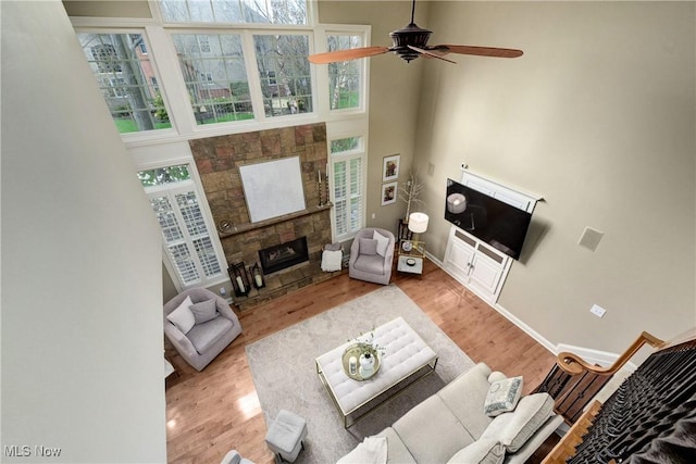 living room with a fireplace, a towering ceiling, a ceiling fan, wood finished floors, and baseboards