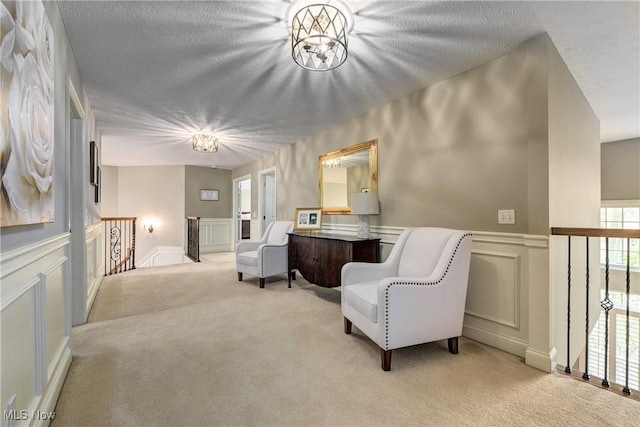 living area featuring a decorative wall, carpet floors, a wainscoted wall, and an upstairs landing