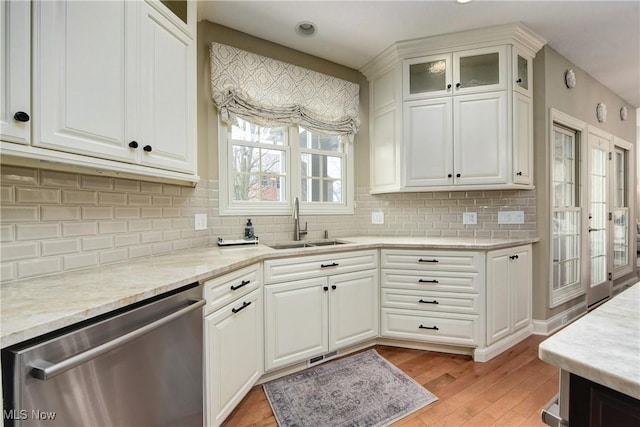 kitchen featuring glass insert cabinets, white cabinetry, stainless steel dishwasher, light wood finished floors, and a sink