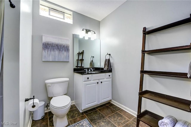 bathroom featuring toilet, vanity, baseboards, and stone finish flooring