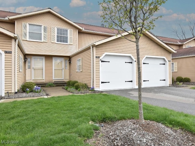 view of property featuring entry steps, an attached garage, a front lawn, and aphalt driveway