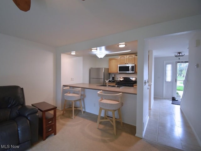 kitchen with a peninsula, light brown cabinetry, a breakfast bar, a sink, and stainless steel appliances