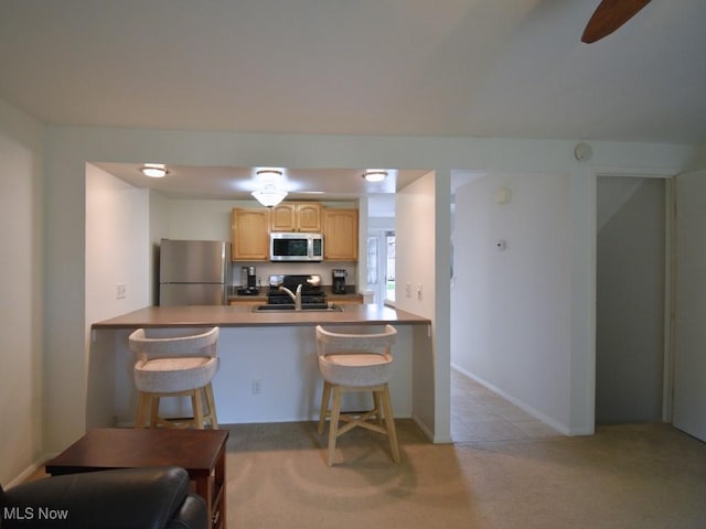 kitchen with a sink, a breakfast bar area, appliances with stainless steel finishes, and light carpet