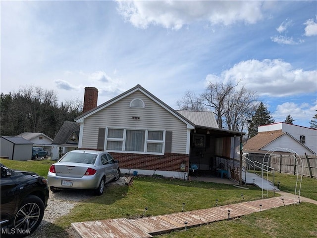 view of front of home with a chimney, a front yard, brick siding, metal roof, and fence