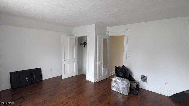 empty room featuring a textured ceiling, wood finished floors, baseboards, and visible vents