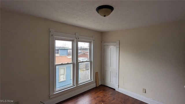 unfurnished room featuring dark wood-type flooring, a textured ceiling, and baseboards