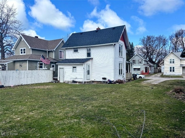 back of house with entry steps, a chimney, fence, and a yard