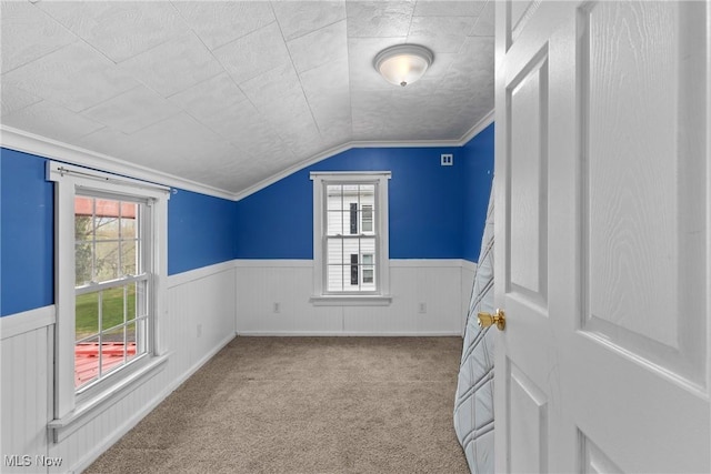 interior space featuring ornamental molding, vaulted ceiling, wainscoting, and carpet