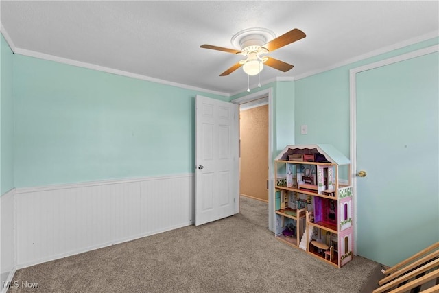 playroom with carpet flooring, wainscoting, ornamental molding, and ceiling fan